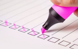 A pink highlighter checking boxes on paper.